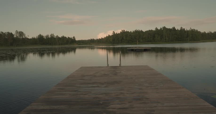 Landscape of a wooden dock in the foreground on the edge of a lake and a dancing forest in the background