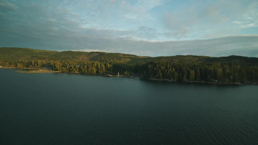 A house with a dock and boat sit on a coastal area near forests and mountains