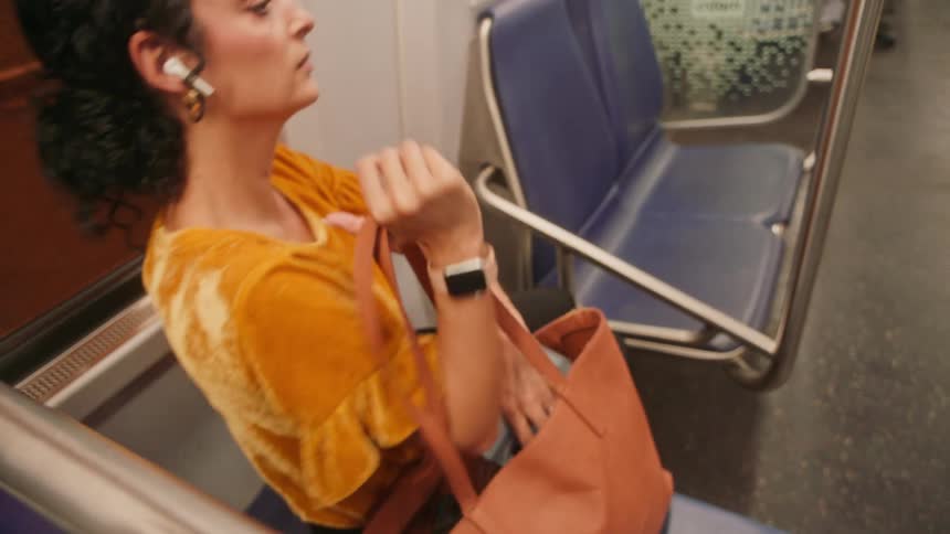 A woman in a yellow shirt sits on a public transit seat looking at her phone then gets up and walks off