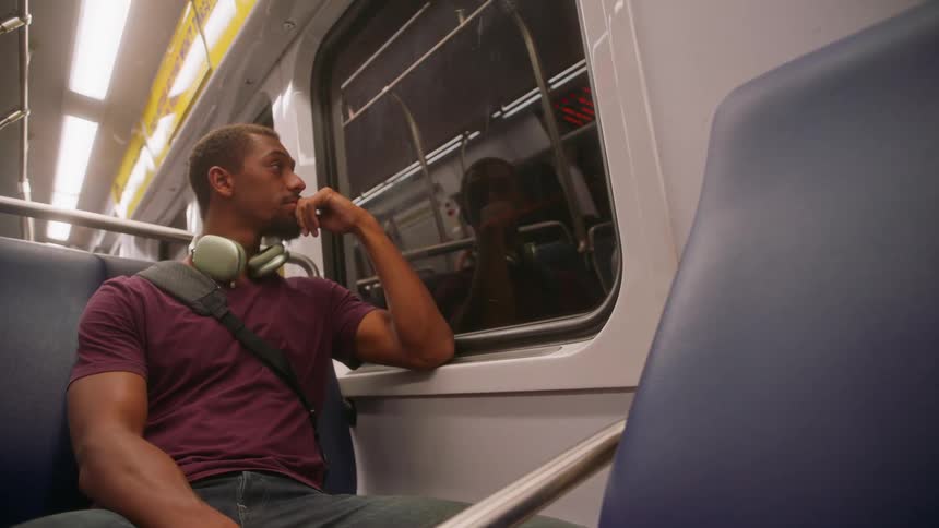Male passenger sitting on a bench of a moving train looking out the window