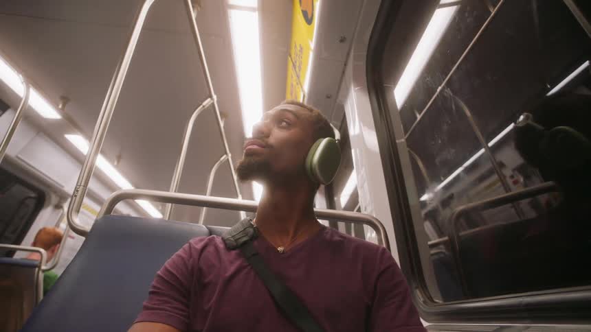 A young man sits inside a public transport vehicle wearing headphones and looking up