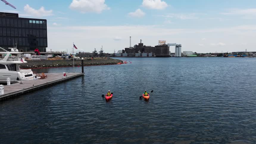 Two kayakers parallel each other while paddling past the marina on a cloudy day