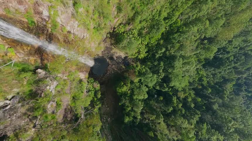 Twisting aerial view of a waterfall cascading down a rocky cliff surrounded by dense green forest