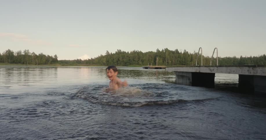Laughing boy jumps off a dock and into the lake to swim
