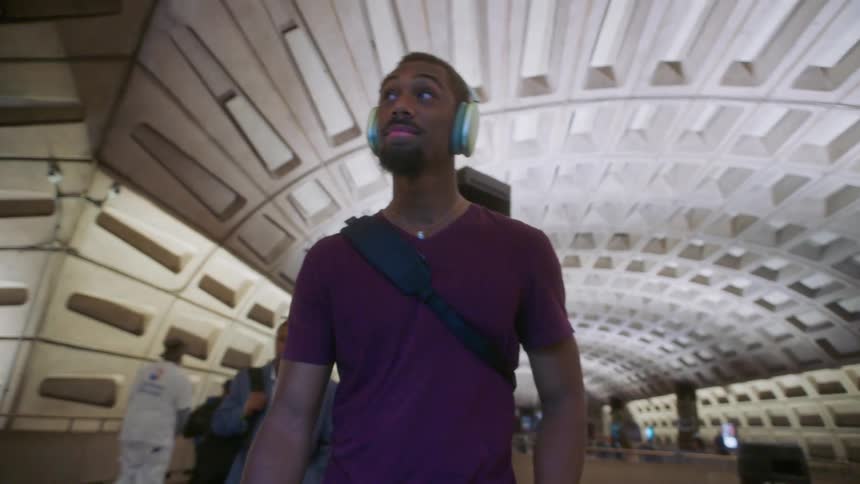 A young man in a subway station walking into the train while listening to music on his headphones