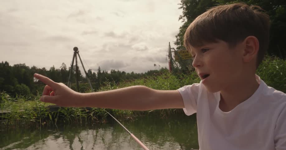 A young boy points while he sits on a dock while fishing