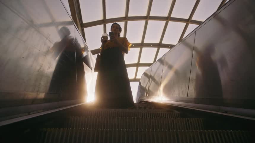 A woman looking at her cell phone as she stands on an escalator going down