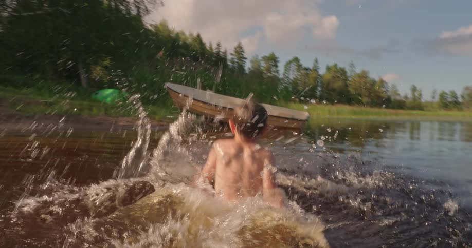 A young boy jumps into a lake from a wooden dock and proceeds to splash around in the water