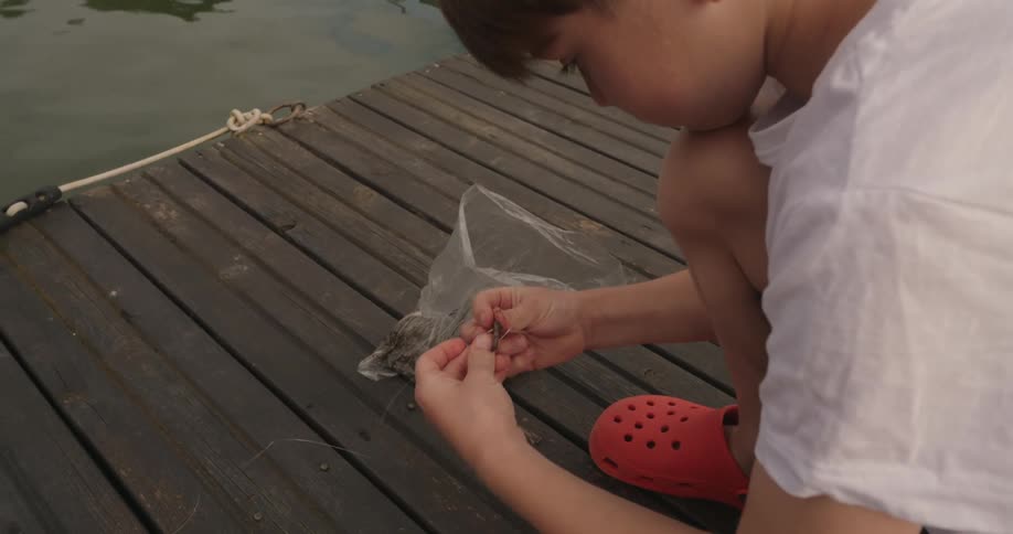 Boy on a dock baiting a fishing line