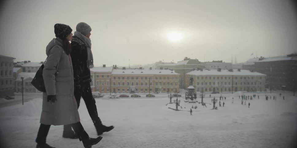 Couple walking together holding hands on a snowy day through the city next to a square
