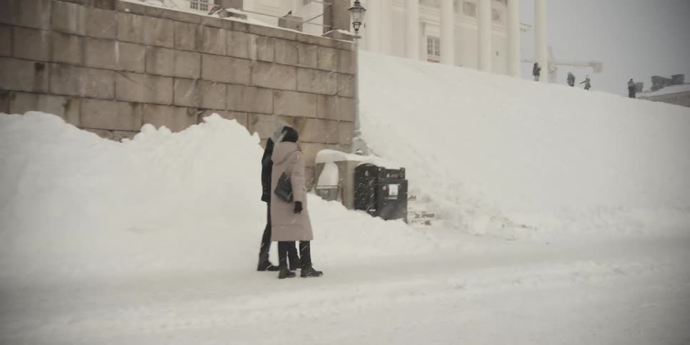 A couple hold hands as they walk on a snowy city street
