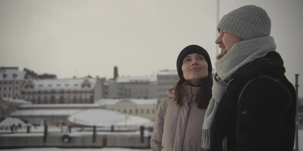 A man and a woman talk to each other while standing outside in falling snow in a city