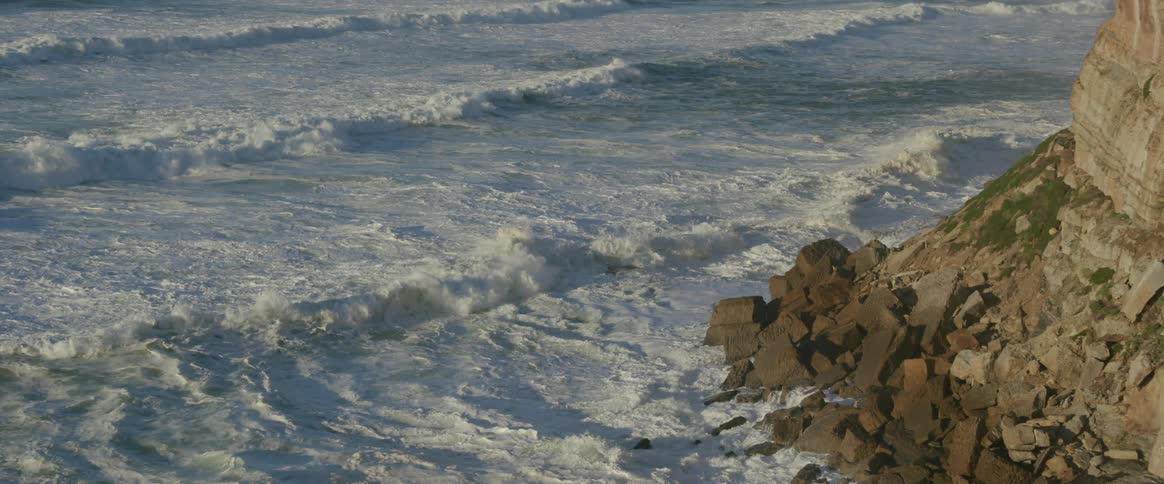 Large foamy waves crash against a rocky coastline
