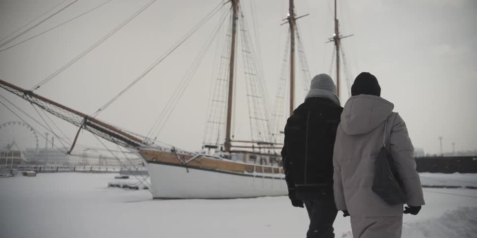 Couple walking hand in hand on a snowy day next to boats