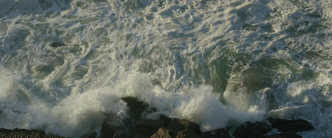 View from above of the strong water with sea foam hitting rocks