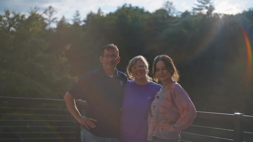 Father mother and daughter hugging on the balcony with trees and sunlight in the background
