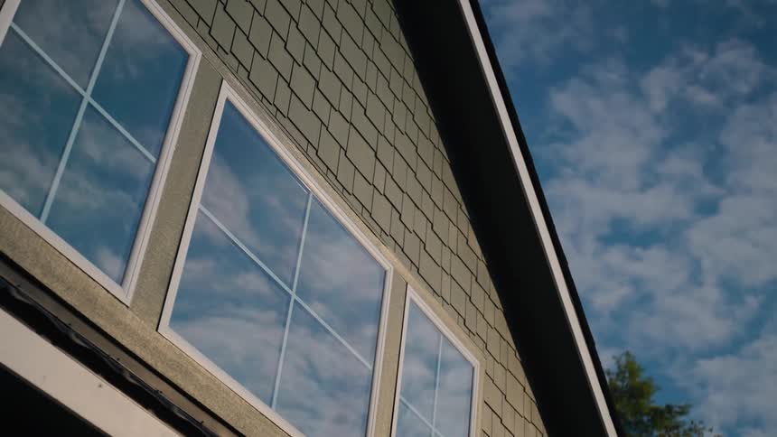 Wispy clouds float in a blue sky over a house with three windows