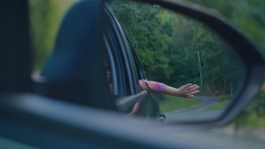 Rear view of a moving car and a teenage girl with one arm out
