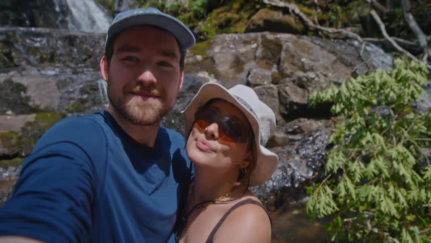 Portrait of a man and a woman kissing while standing next to a waterfall in a natural setting
