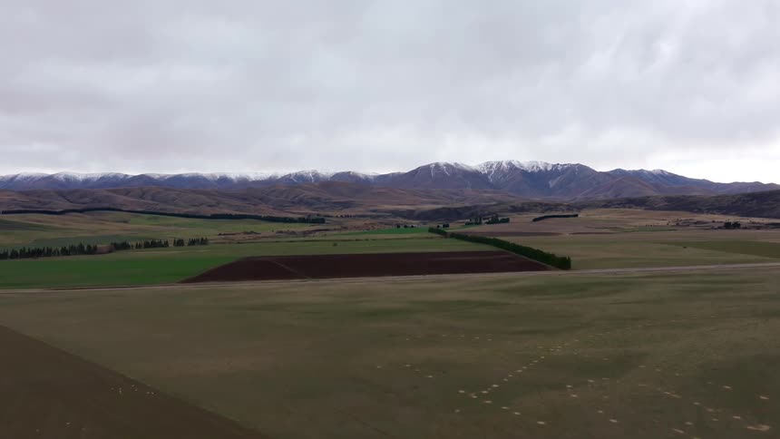 Flying across far fields with mountain range far in the distance