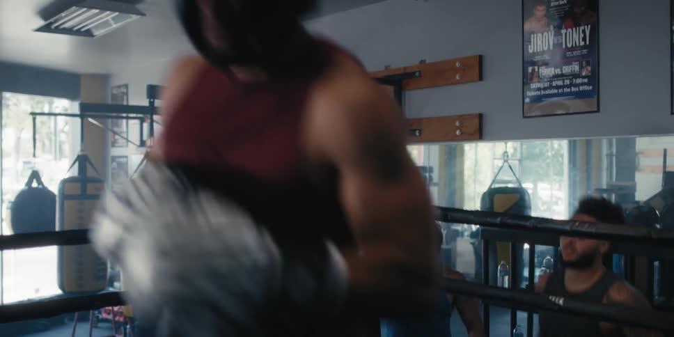 A corner man helps a strong muscular boxer get inside a ring in a gym