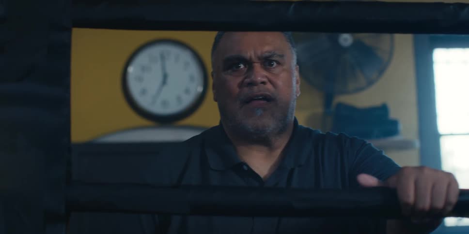 Closeup of a man standing next to a boxing ring watching a fight inside the ring