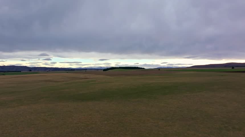 A vast open field under an overcast sky with distant low hills on the horizon