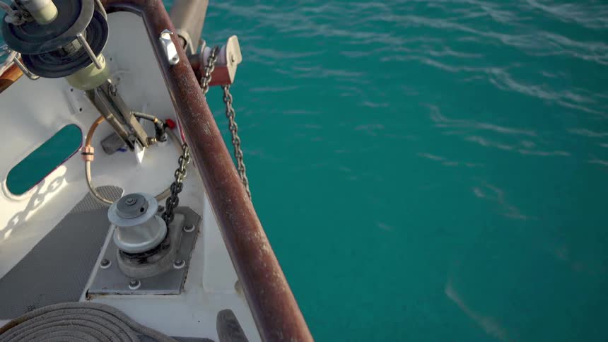 A sailboat dropping anchor into clear turquoise water
