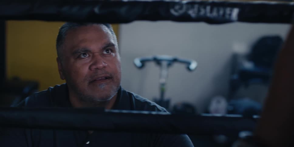 Closeup of a boxing coach standing next to a boxing ring talking to a boxer inside the ring