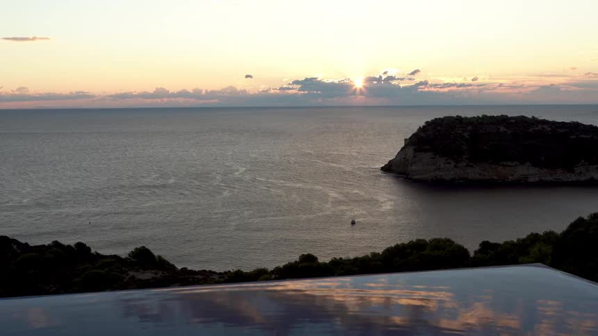 Sun sits near a red horizon while ripples flow across a seaside swimming pool