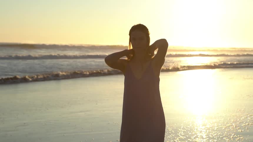 A woman on a white dress walking on a beach with the ocean in the background during sunset