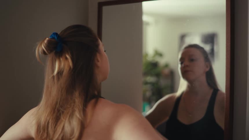 A woman tying her hair up in front of a mirror