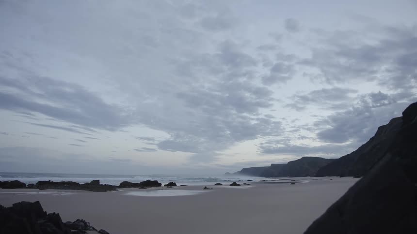 Ocean waves roll into a sandy beach on a mostly cloudy day