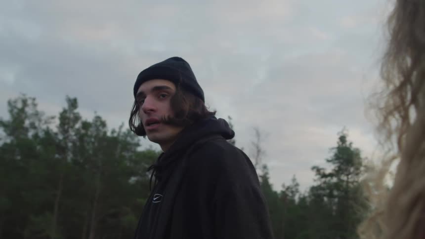 A young man with long hair wearing a hoodie walks away from a woman