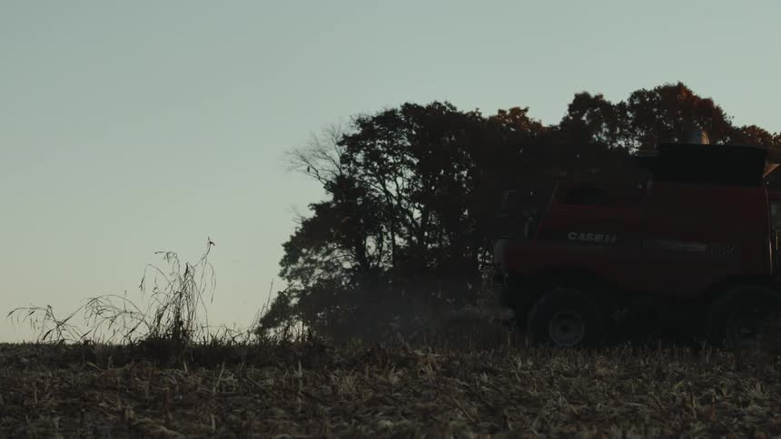 A combine harvester at work in a field during dusk