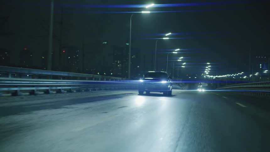 Car driving on a paved street at night with buildings of a metropolis in the background