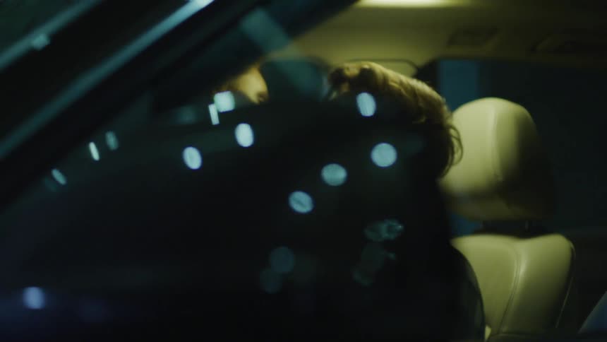 Couple kissing inside parked car at night with woman on top of man