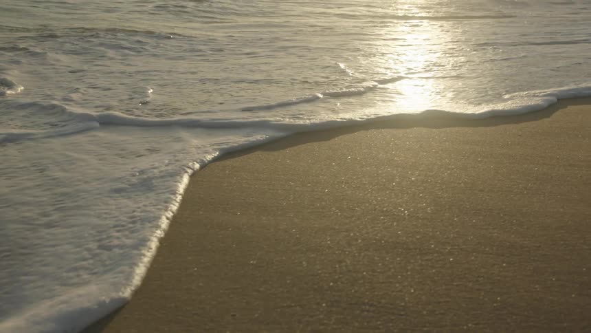 Sunlight shines upon the water as waves roll in over the beach