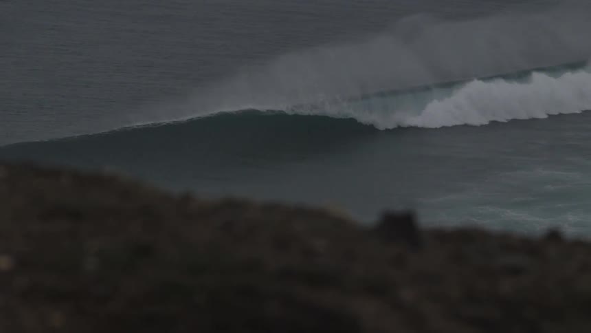 An extremely large wave crests off of a coastline