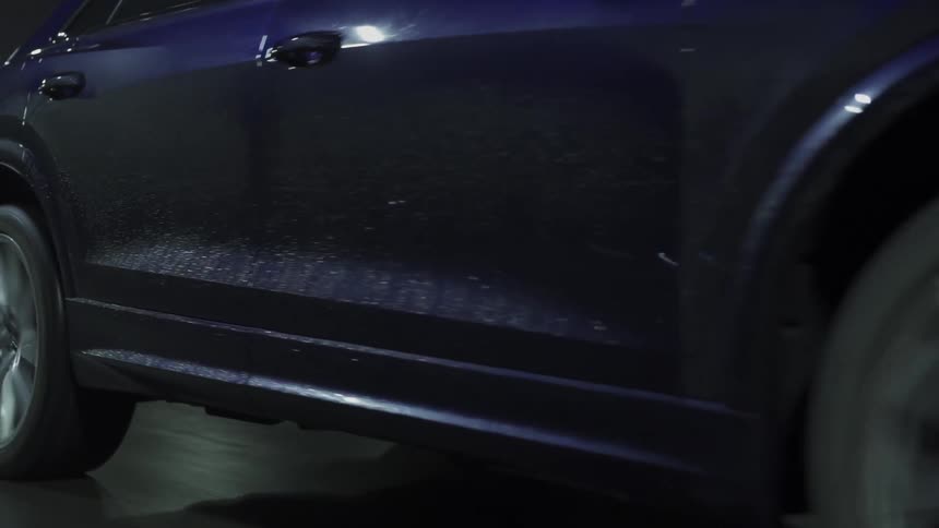 A black car with its headlights on drives down a road at night
