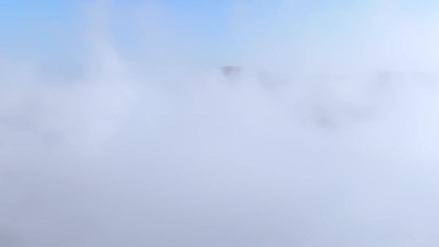 A landscape view of green hills partially covered by a layer of white clouds with a clear blue sky above