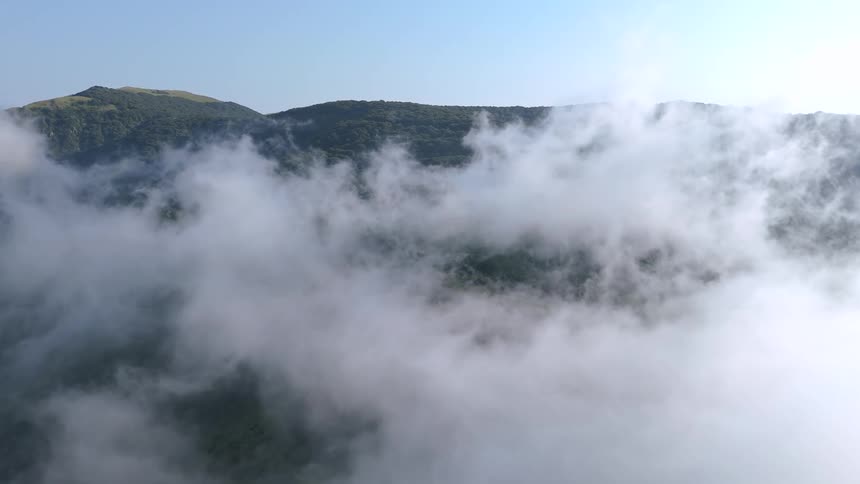 An aerial view of a large white cloud in an area with a huge hill in the background