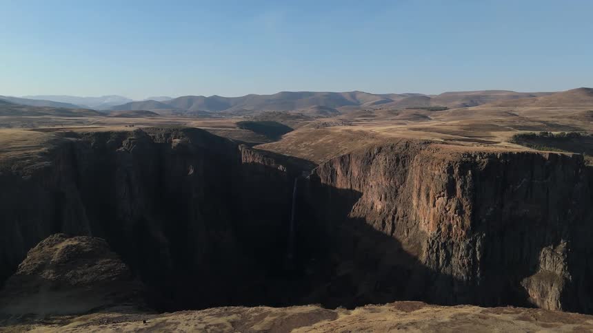 A vast canyon with steep cliffs on a rugged desert terrain under a clear sky