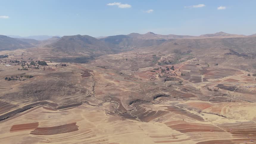 Arid landscape with terraced fields and rolling hills under a clear blue sky
