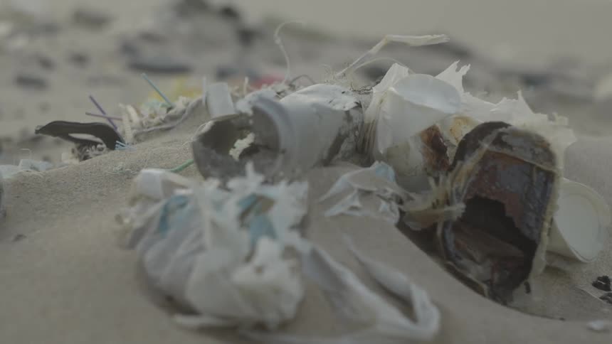 Wind flutters plastic bags lying on the sand amongst other trash