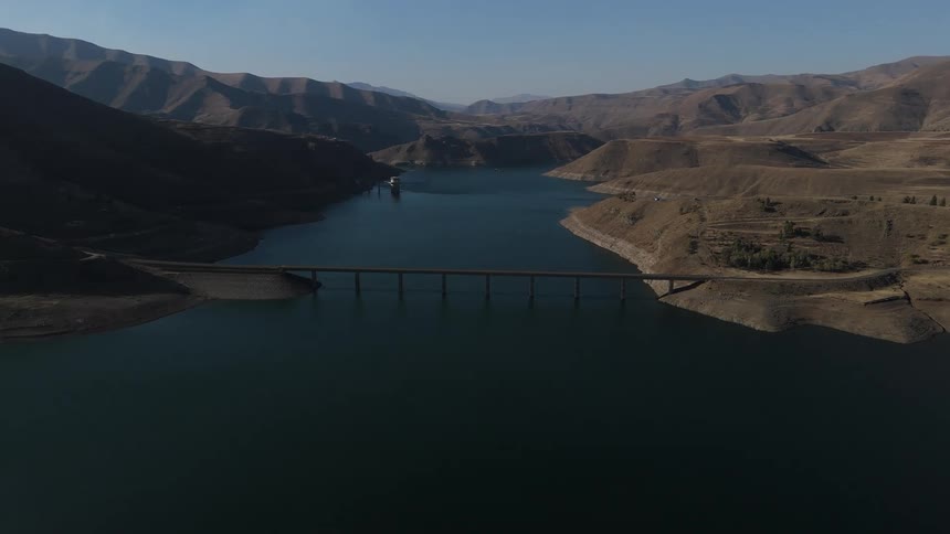 Aerial view of a bridge over a river connecting rocky terrain with mountains in the background