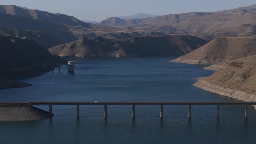 A bridge spans across a body of water with arid hills surrounding the area
