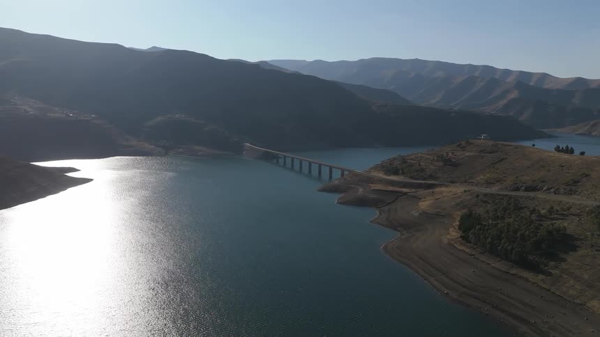Aerial view of a long bridge in the background connecting mountains and above a reservoir