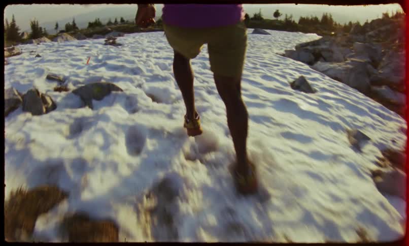 Man wearing shorts runs across patches of snow on a cloudy day