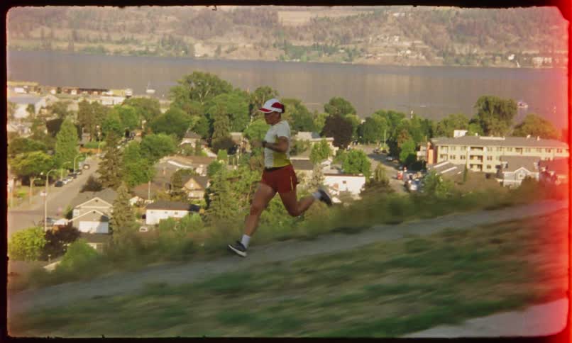 Person running on a grassy slope with a body of water and buildings in the background